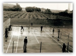 Czarno-biała fotografia kortu tenisowego. Grupa uczniów grająca w tenisa. 